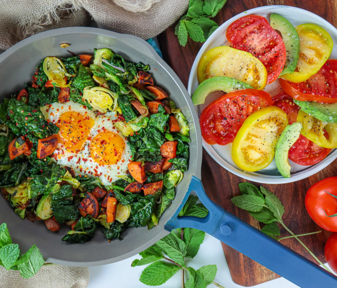 Breakfast sweet potato hash in a pan with brussel sprouts, sunnyside eggs, and colorful tomatos.